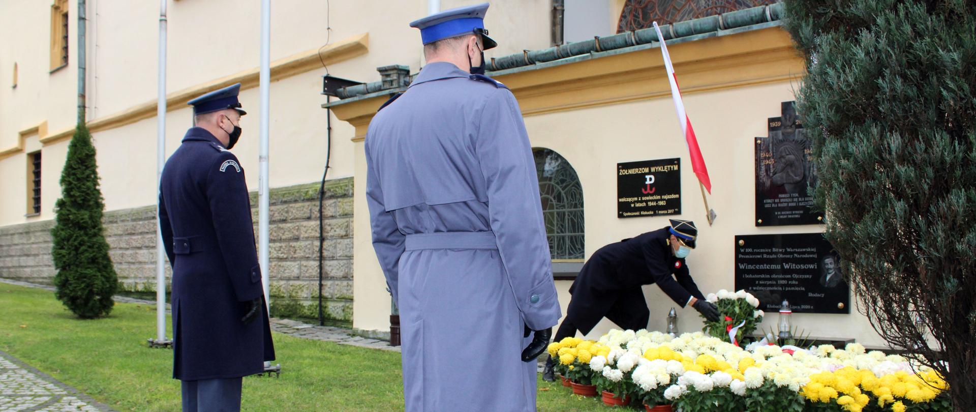 Zdjęcie przedstawia złożenie przez Komendanta Powiatowego Państwowej Straży Pożarnej w Kłobucku st. bryg. Roberta Ladra wraz z przedstawicielami służb mundurowych: Komendantem Powiatowym Policji w Kłobucku insp. Tomaszem Górka oraz Komendantem Centralnego Ośrodka Szkolenia Służby Więziennej w Kulach ppłk. Dariuszem Małolepszym kwiatów pod pamiątkową tablicą marszałka Józefa Piłsudskiego