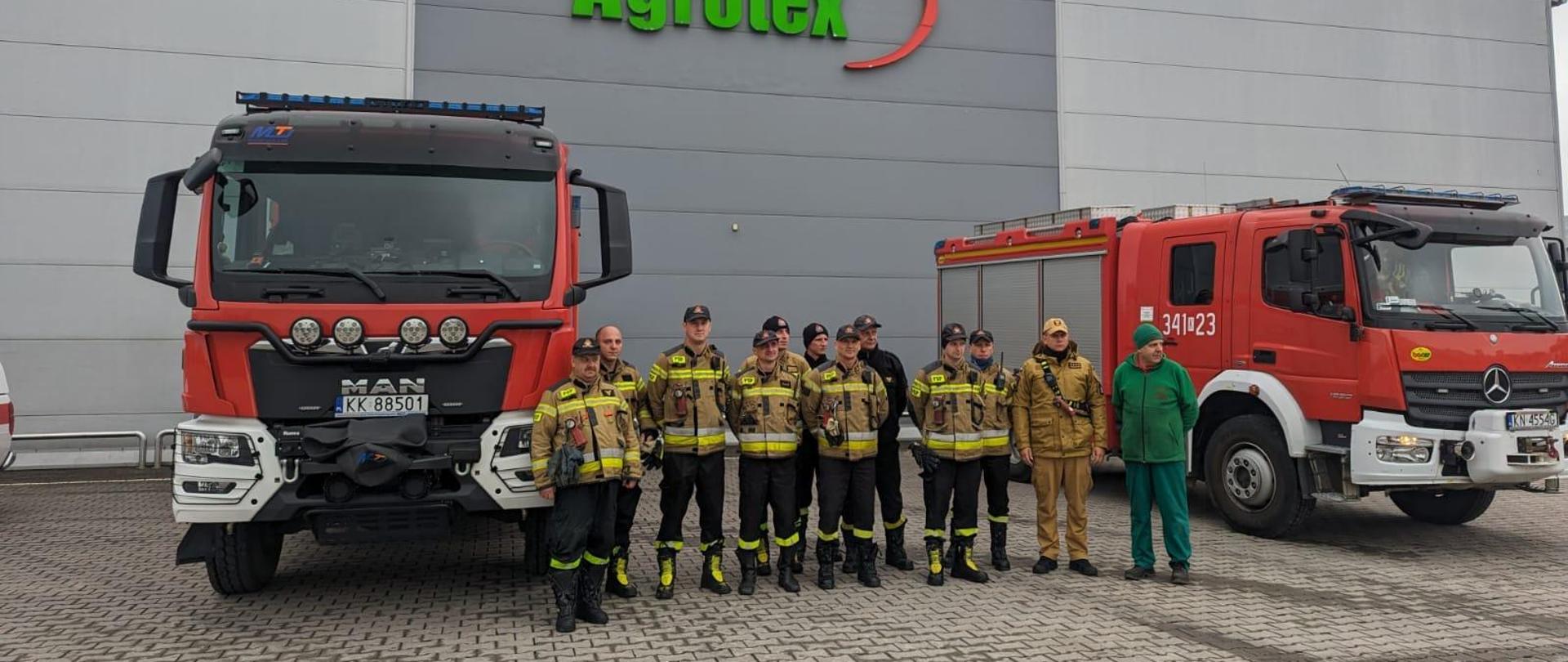 Strażacy obok samochodów pożarniczych przed zakladem