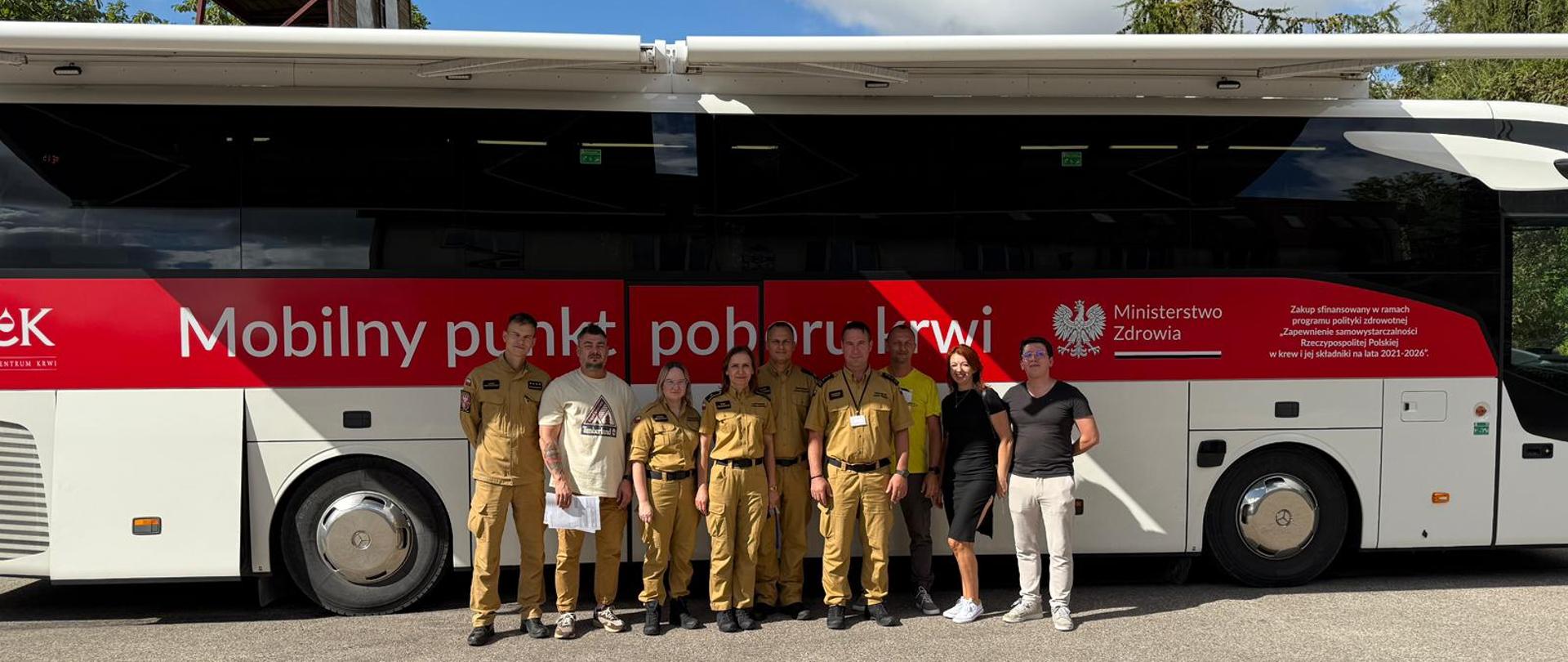 Funkcjonariusze Komendy wraz z uczestnikami akcji pobrania krwi na tle autobusu. 