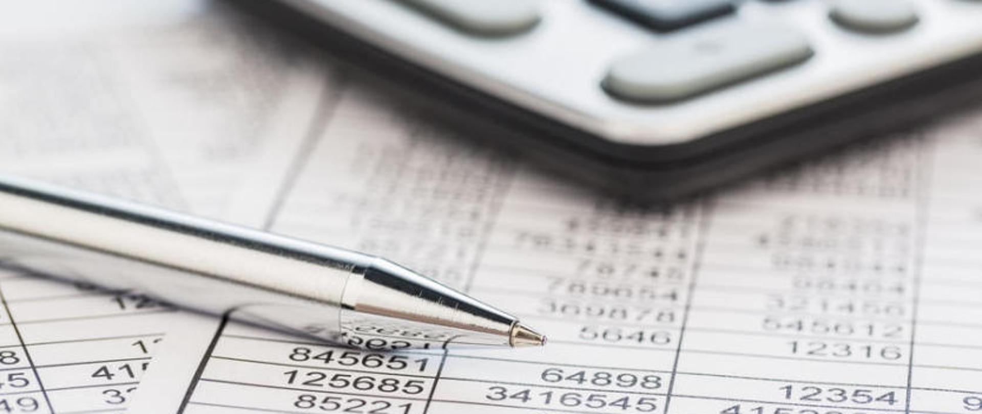 Długopis i klawiatura leżące na zapisanej cyframi kartce papieru