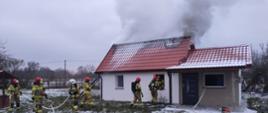 Na zdjęciu budynek który się pali strażacy wchodzący do budynku w aparatach OUO rozwinięte linie gaśnicze i wentylator 