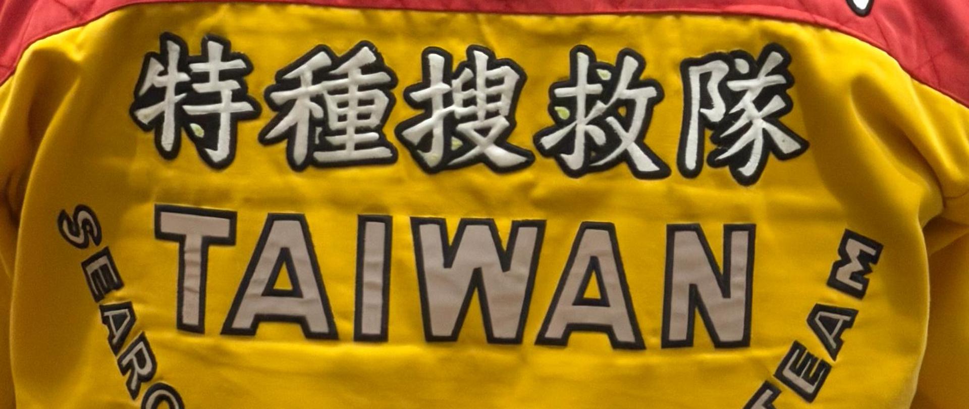Zbliżenie na tył żółto-czerwonej kurtki ratowniczej z napisami w języku chińskim oraz angielskim „TAIWAN Search & Rescue Team”.