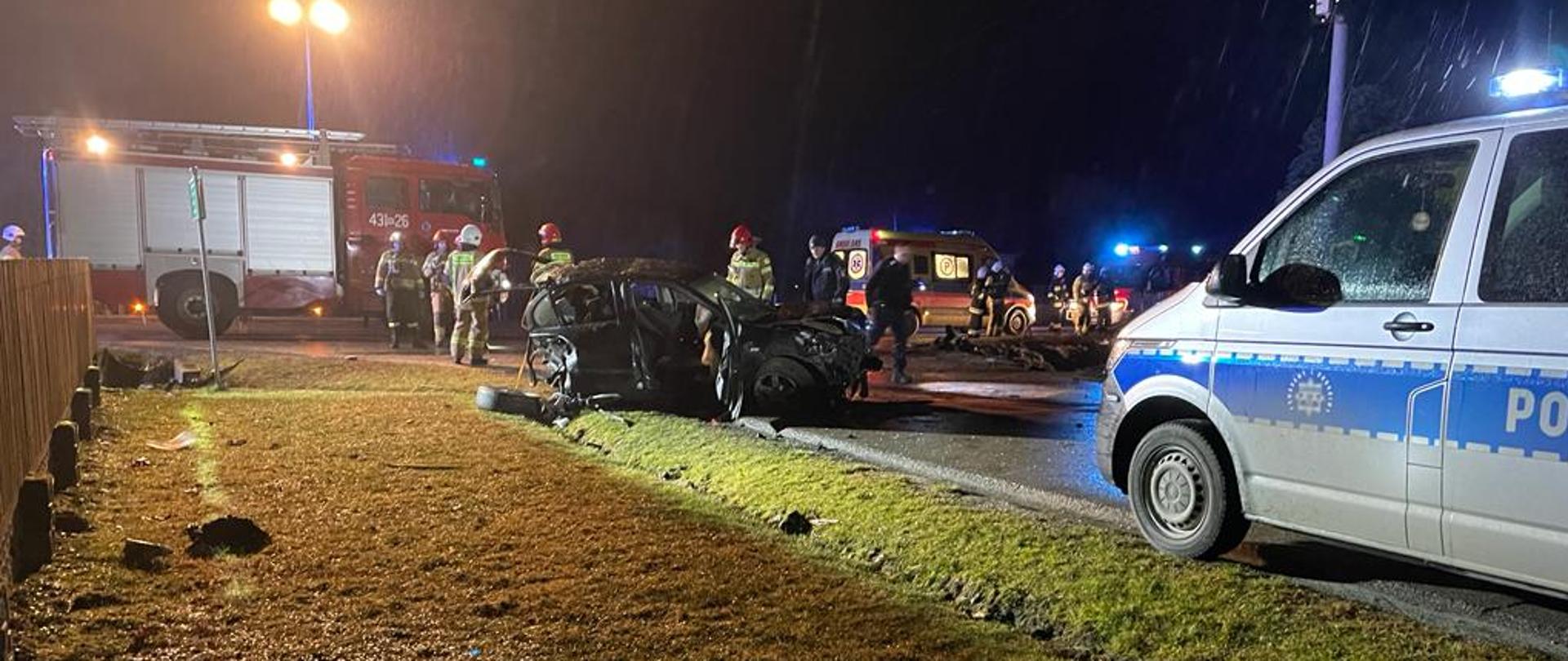 Na zdjęciu rozbity samochód na drodze, w tle widać strażaków.