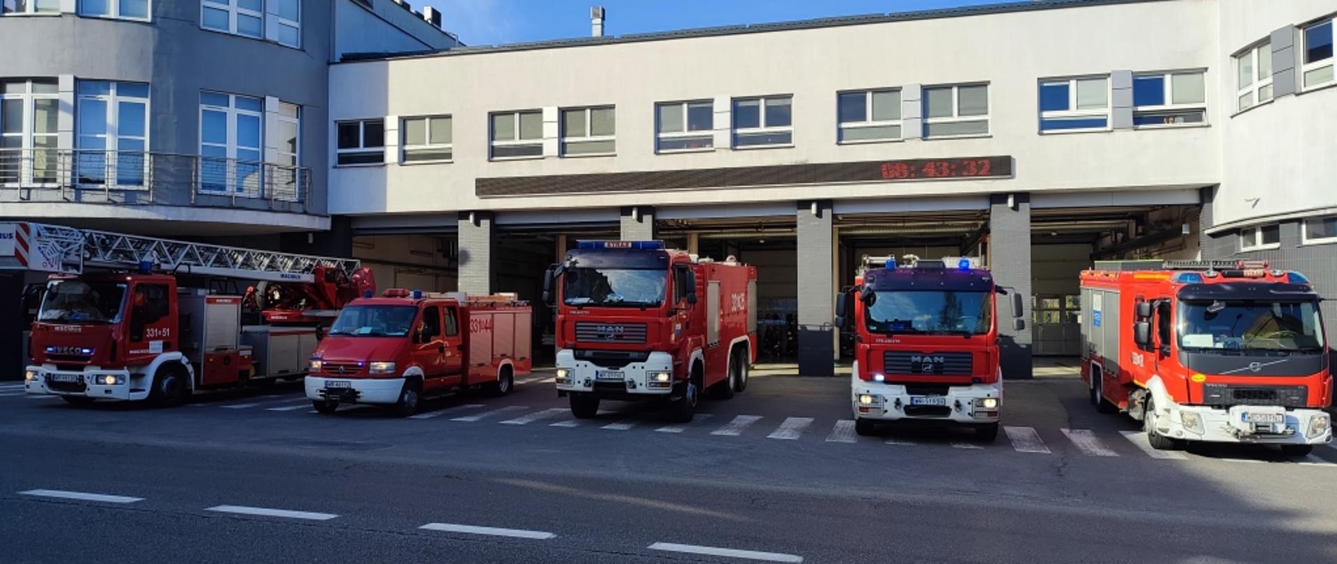 Zdjęcie wykonane przed jednostką ratowniczo – gaśniczą numer 1 w Radomiu. Na zdjęciu widać ustawione przed jednostką pojazdy ratowniczo - gaśnicze. Pojazdy mają włączone alarmowe sygnały świetlne i dźwiękowe. Strażacy upamiętniają ofiary katastrofy lotniczej pod Smoleńskiem.