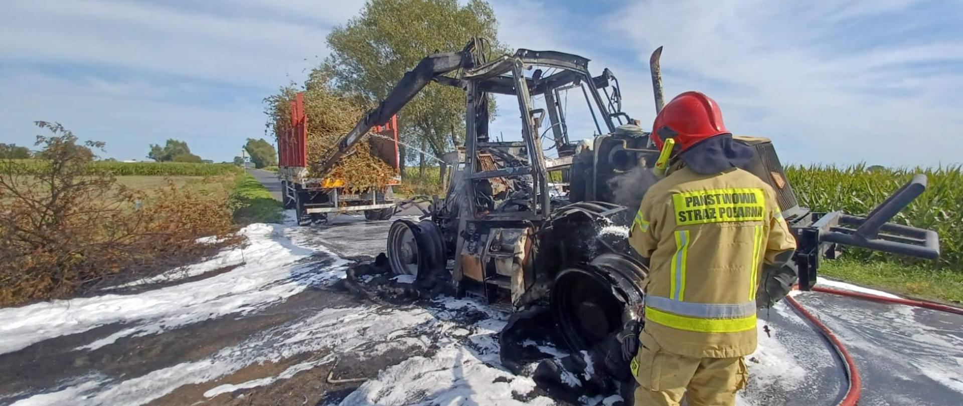 Na zdjęciu widać spalony ciągnik rolniczy oraz strażaka.