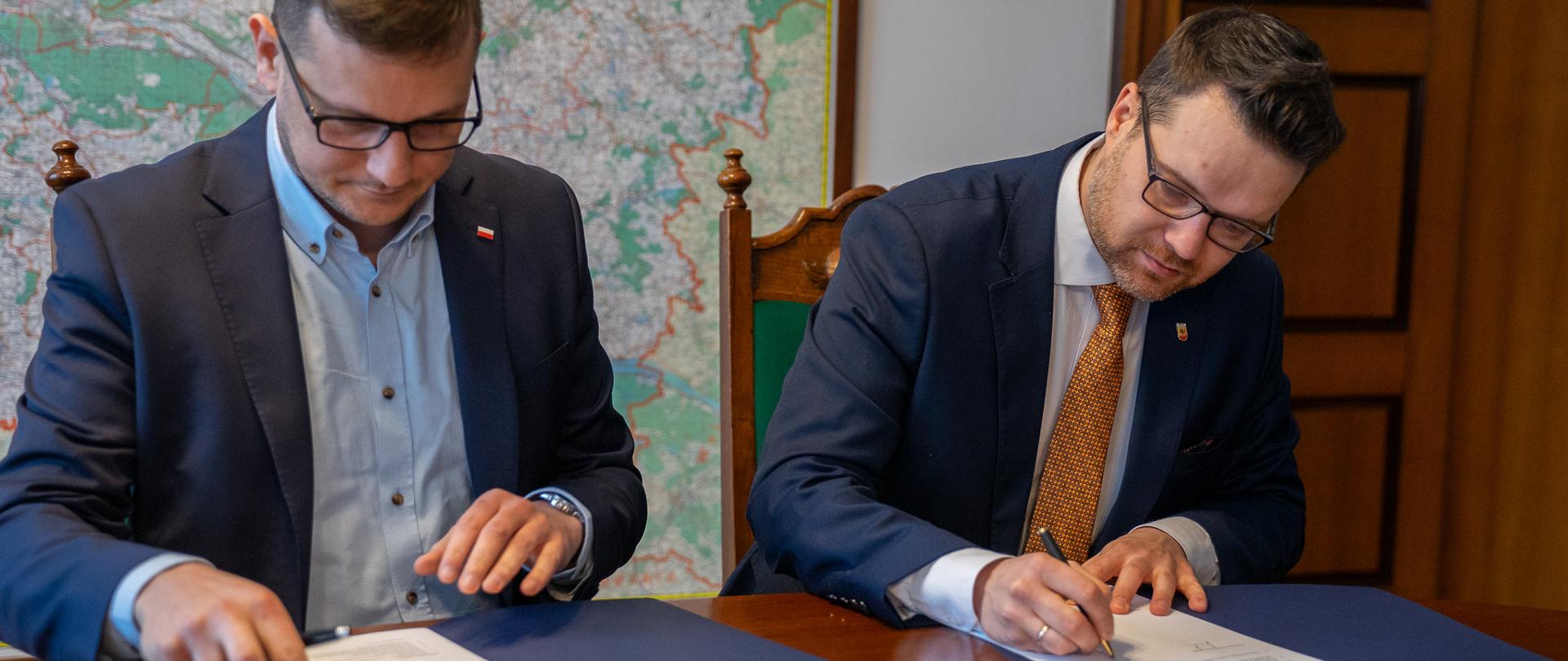 Wojewoda Michał Sztybel oraz Starosta Bydgoski Piotr Kozłowski siedzą przy stole i podpisują umowę na dofinansowanie inwestycji w ramach Rządowego Funduszu Rozwoju Dróg (RFRD).