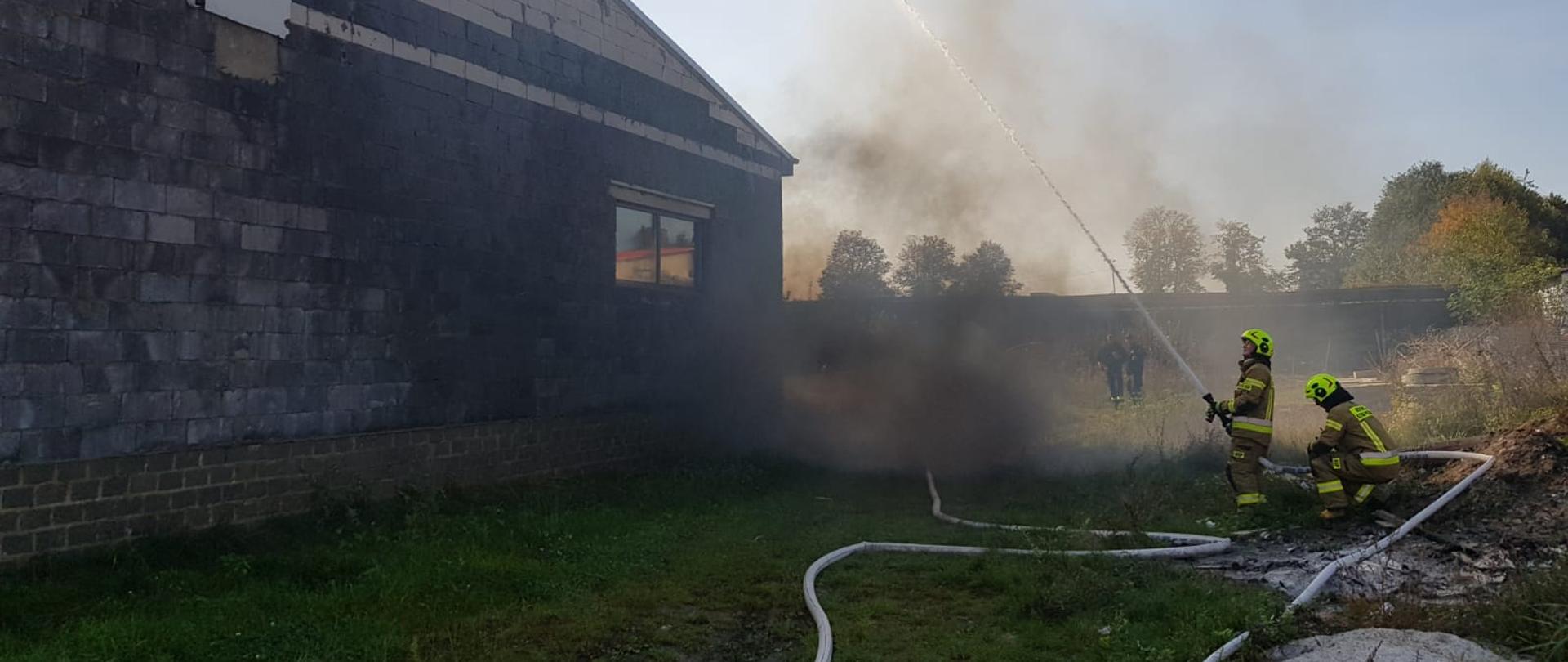 Widoczni strażacy podczas ćwiczeń, podający prąd gaśniczych z zewnątrz.