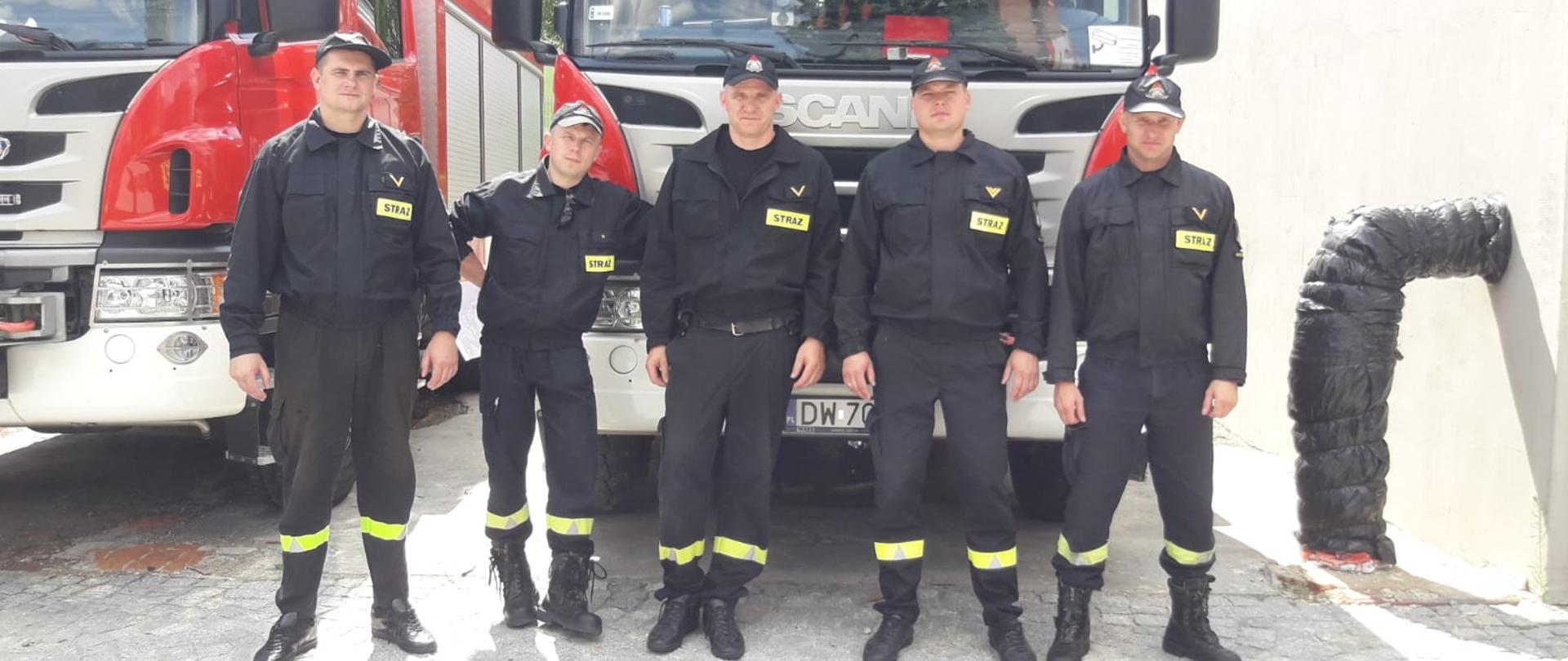 na tle pojazdu strażackiego stoi pięciu strażaków w mundurach 