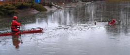Na zdjęciu widać dwóch strażaków ubranych w ubrania do ratownictwa wodno-lodowego. Jeden z strażaków znajduje się w wodzie udając osobę poszkodowaną, drugi zaś dopływa do niego na saniach lodowych. W tle infrastruktura OSIR "Gutwin"