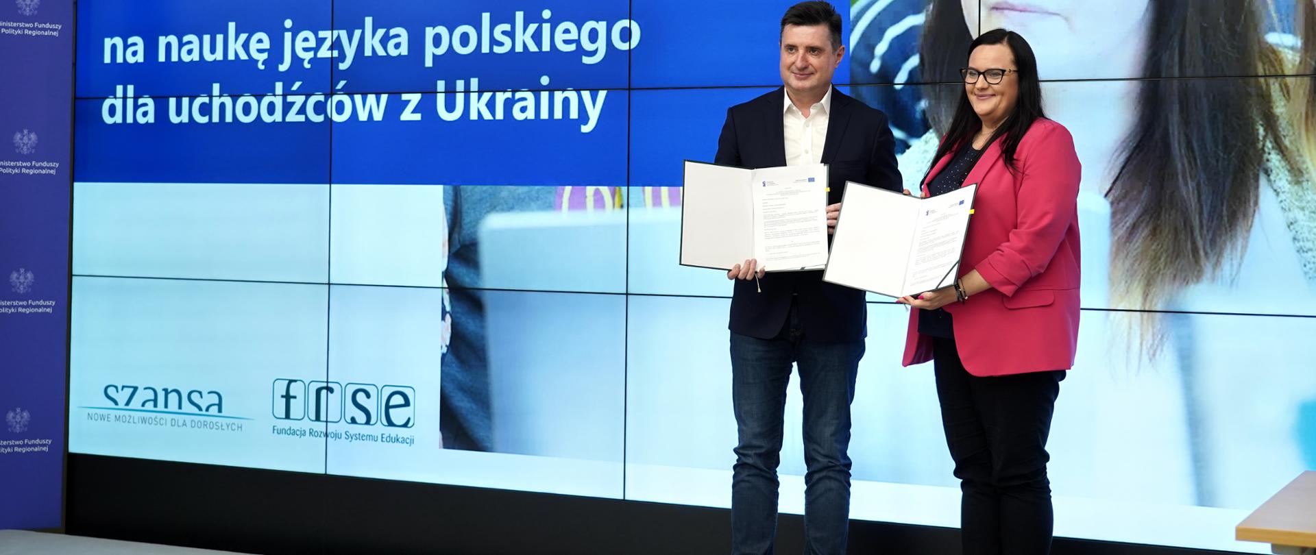 W sali konferencyjnej wiceminister Małgorzata Jarosińska-Jedynak i dyrektor Paweł Poszytek pozują do zdjęcia z dokumentami. W rękach trzymają dokumenty.