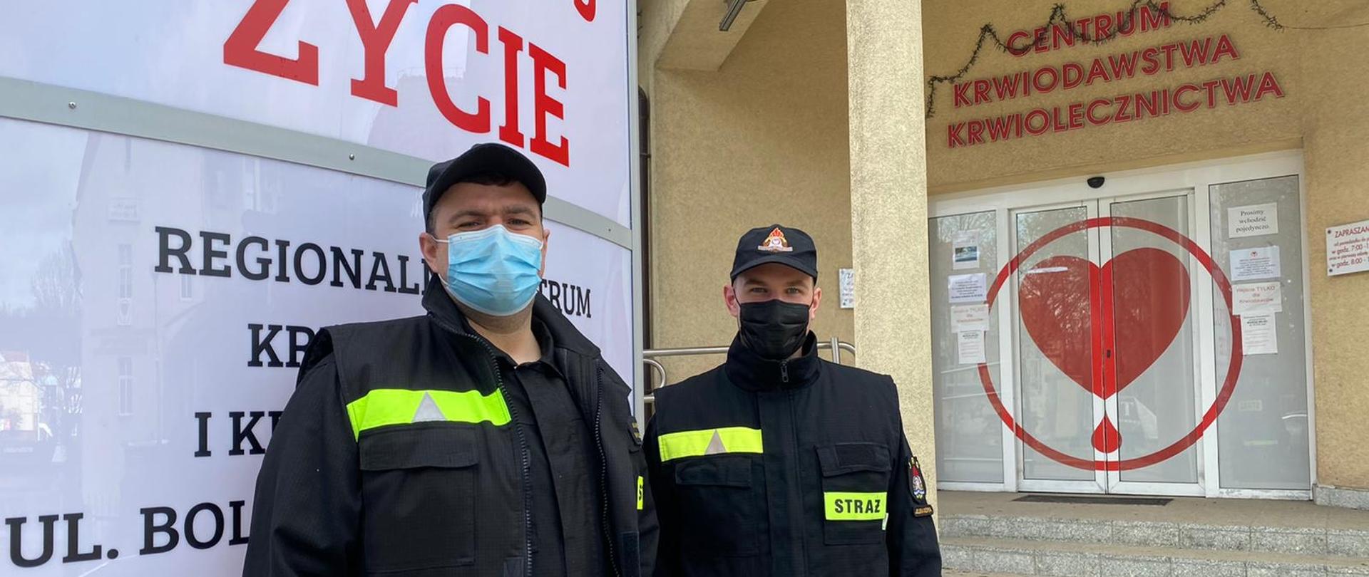Dwóch mężczyzn - strażaków stoi w mundurze przed wejściem do szpitala