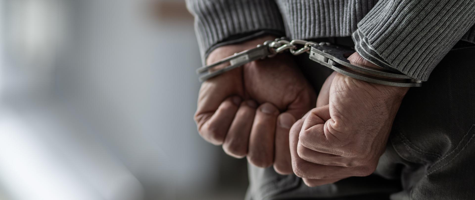 postać człowieka tyłem, ręce skute kajdankami