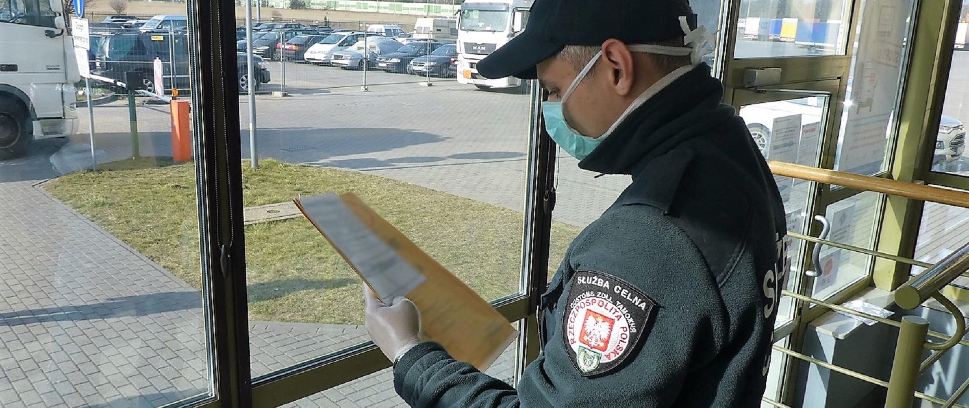 Funkcjonariusz KAS w masce antybakteryjnej i rękawiczkach przegląda dokumenty.