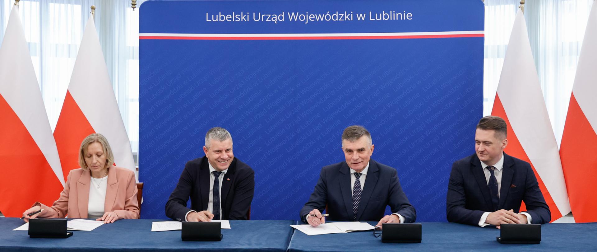 Wojewoda i samorządowcy za stołem prezydialnym. Podpisują umowy. 