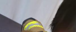 Obraz przedstawia strażaka uwalniającego dziecko z nałożoną nakładką sedesową na szyi