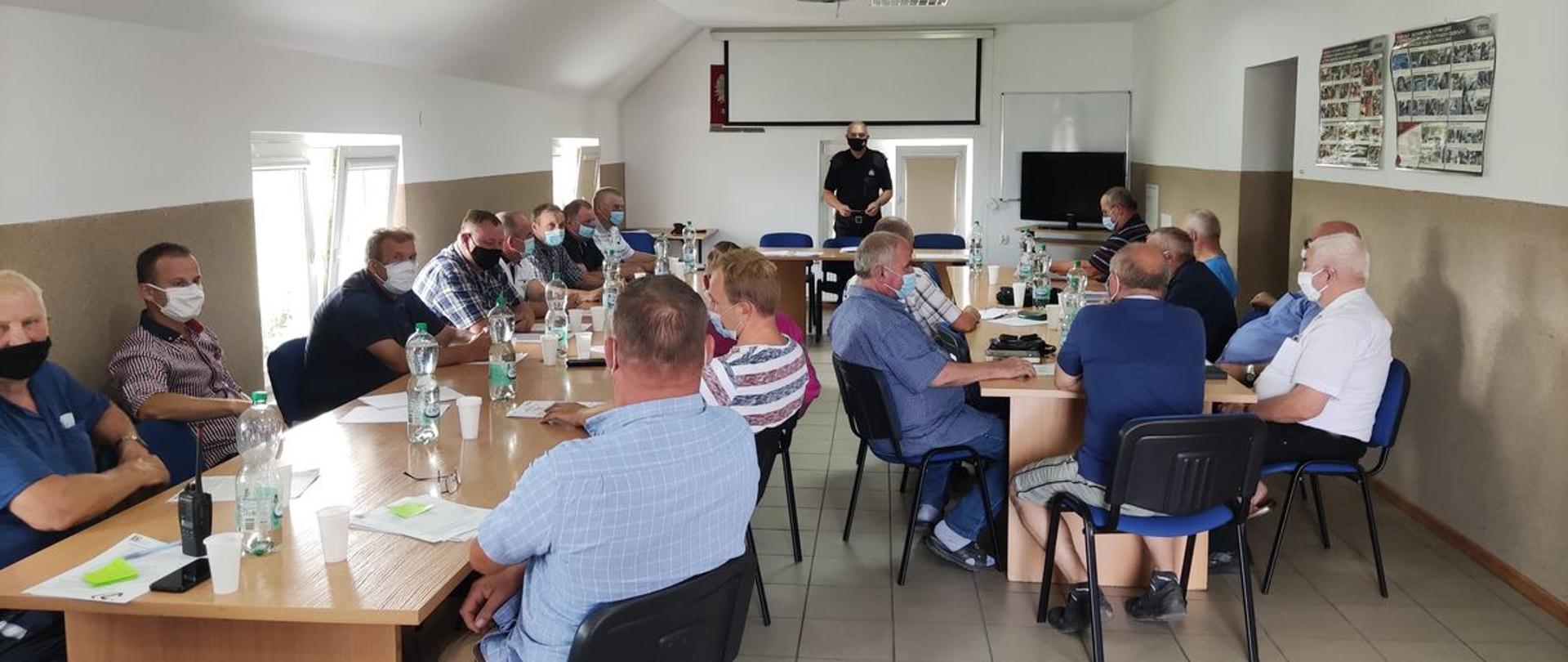 Zdjęcie przedstawia świetlicę KP PSP w Radziejowie od wewnątrz, w której zgromadzeni przy stołach siedzą przedstawiciele ochotniczych straży pożarnych z terenu powiatu radziejowskiego, przed nimi omawiający program SzczepimySię z OSP mł. bryg. Jarosław Stokwisz – Zastępca Komendanta Powiatowego PSP w Radziejowie.