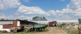 Zdjęcia w ciągu dnia. Widać teren działań ratowniczo-gaśniczych, samochód specjalny w kolorze czerwonym. W tle zabudowania gospodarcze, tunel foliowy oraz silos.