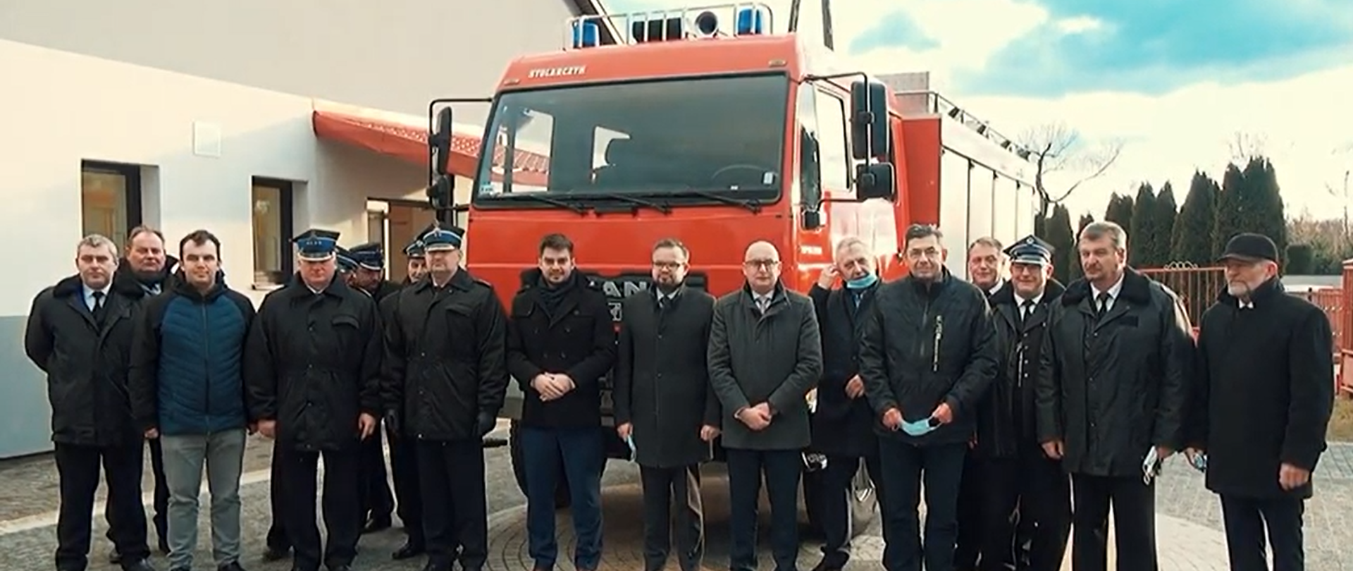 Goście zaproszeni stoją w rzędzie przed przekazywanym samochodem ratowniczo - gaśniczym