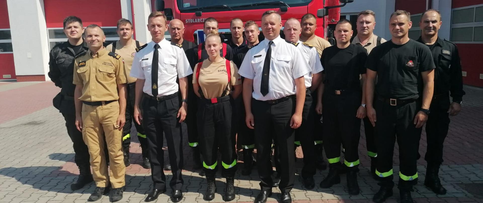 Zdjęcie przedstawia strażaków stojących na placu jednostki ratowniczo - gaśniczej przed samochodem strażackim