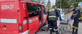 Na zdjęciu druhowie pomagający w transporcie seniorki do punktu szczepień . Pomagają przy wsiadaniu do pojazdu