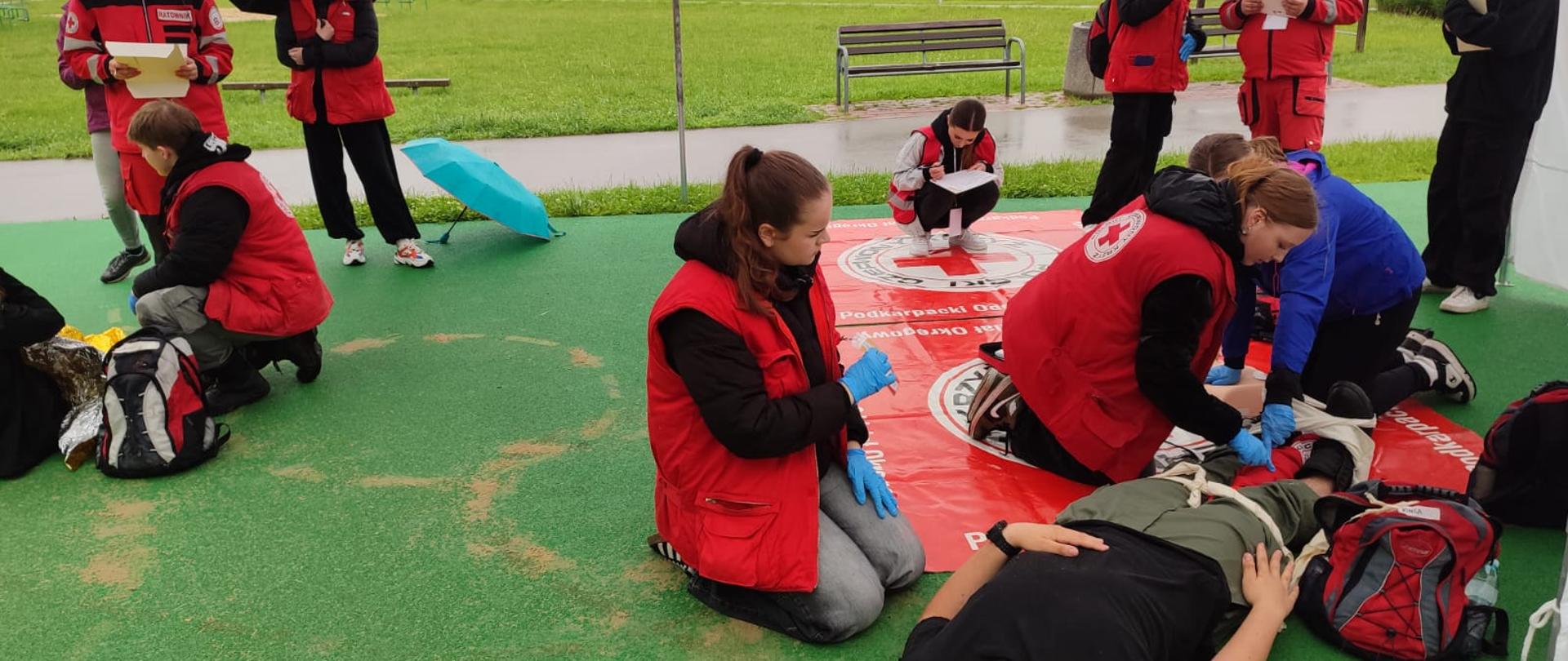 XXXI Mistrzostwa Pierwszej Pomocy PCK etap okręgowy. Na zdjęciu widać poszkodowanych, którzy są opatrywani przez ratowników. Widać sędziów, którzy przyglądają się pracy ratowników i ich oceniają. 