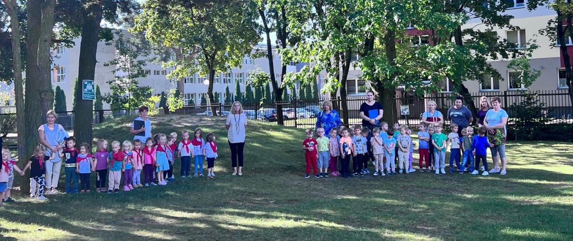 przedszkolaki wraz z opiekunami stoją na placu zabaw podczas próbnej ewakuacji