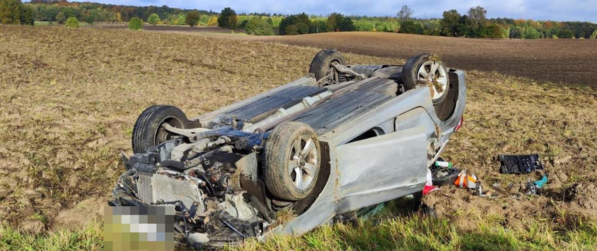 Kolizja samochodu osobowego przy miejscowości Przyjezierze - pojazd koloru srebrnego leży na polu przewrócony na dach