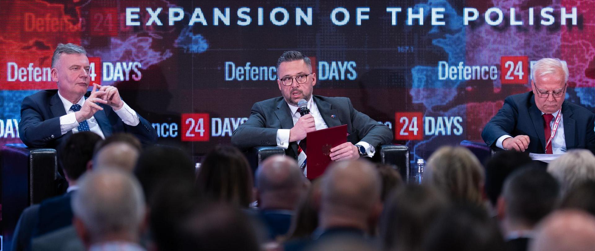 Na scenie siedzi trzech panelistów, wśród nich m.in. wiceminister Marcin Kulasek. Ujęcie zza słuchaczy. W tle ścianka z napisem Expansion of the polish.