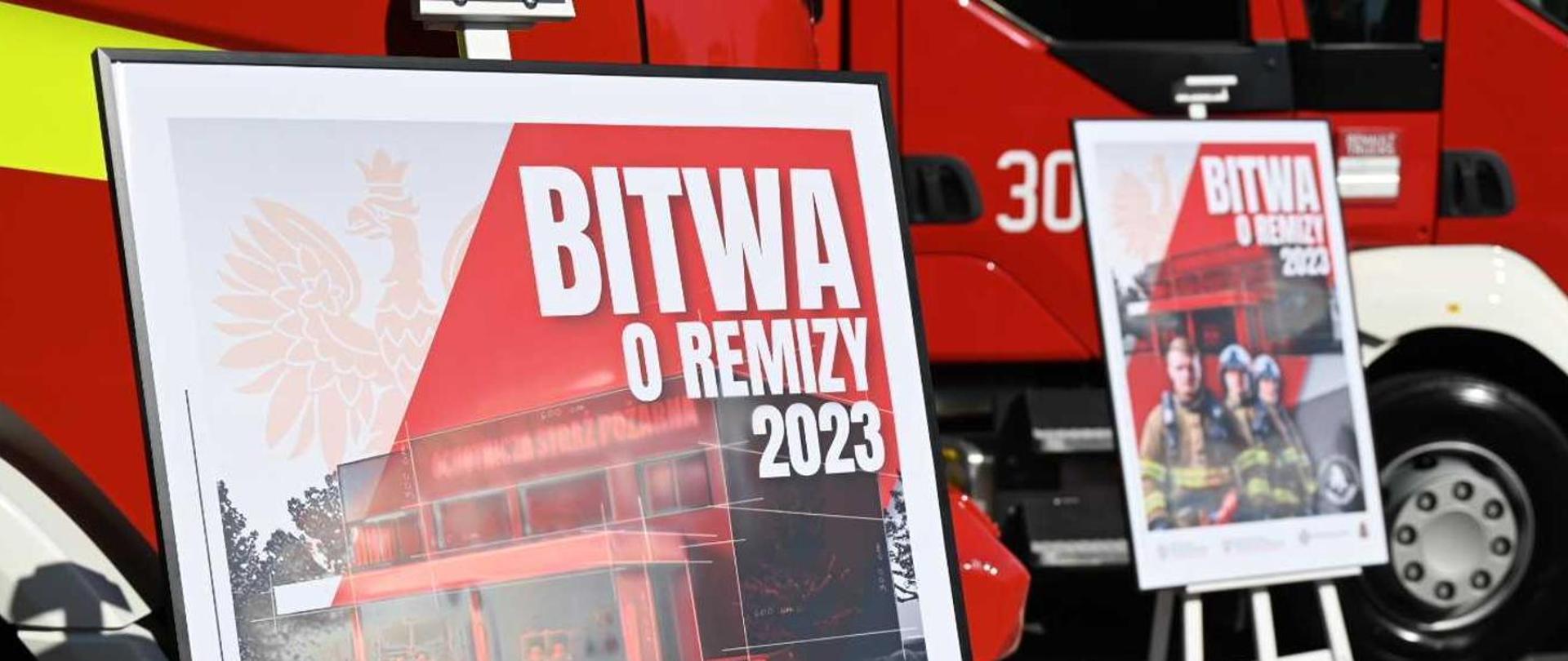 Dwa plakaty promocyjne akcji "Bitwa o Remizy 2023" na tle dwóch pojazdów pożarniczych