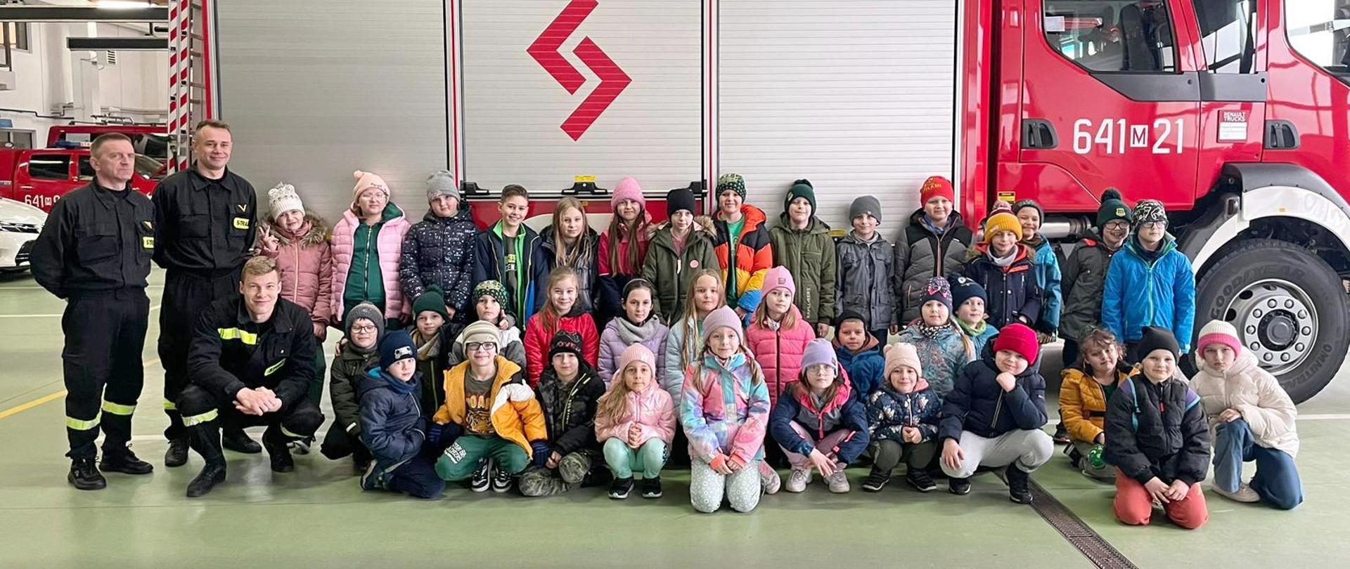 Odwiedziny strażnicy i sali edukacyjnej „Ognik” w KP PSP w Sokołowie Podlaskim 20.03.2024 r. - wspólne zdjęcie w garażu na tle samochodu strażackiego