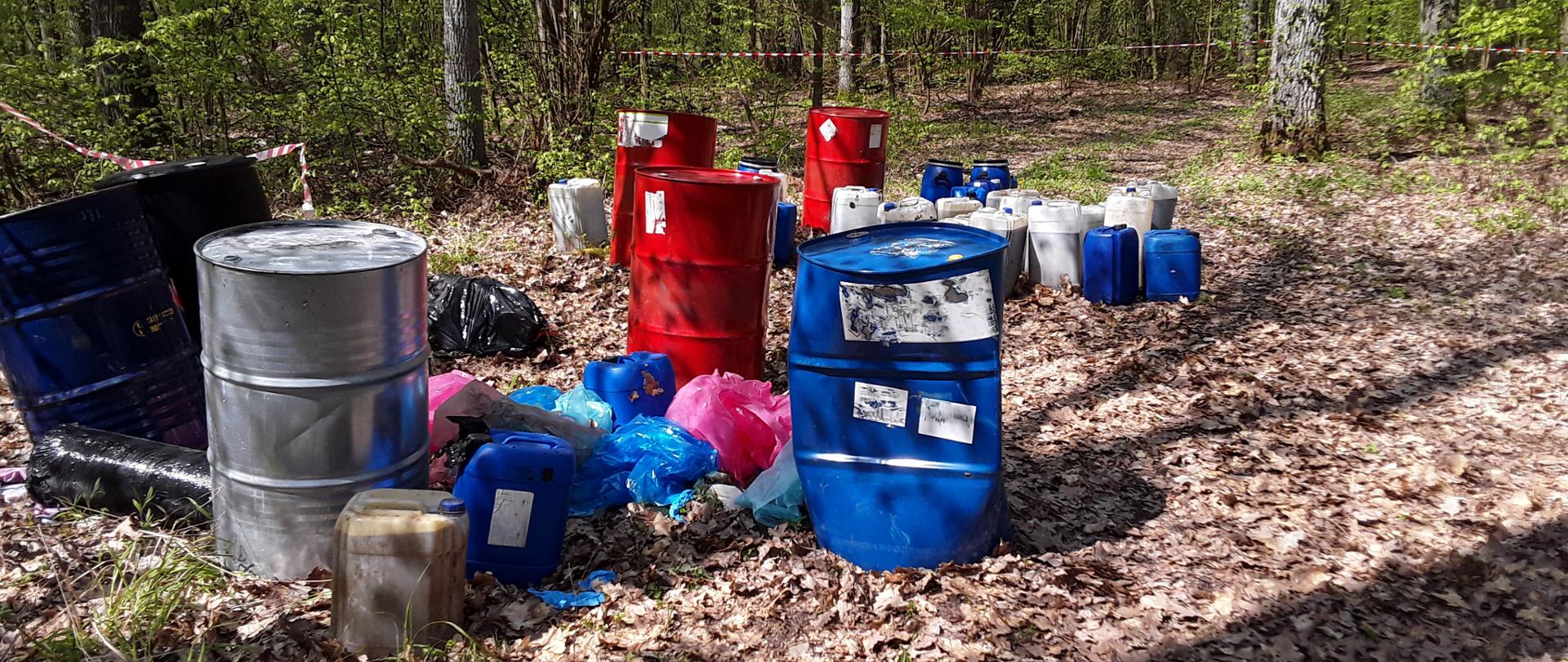 Beczki i kanistry o różnej pojemności z odpadami nielegalnie zgromadzone na otwartym terenie.