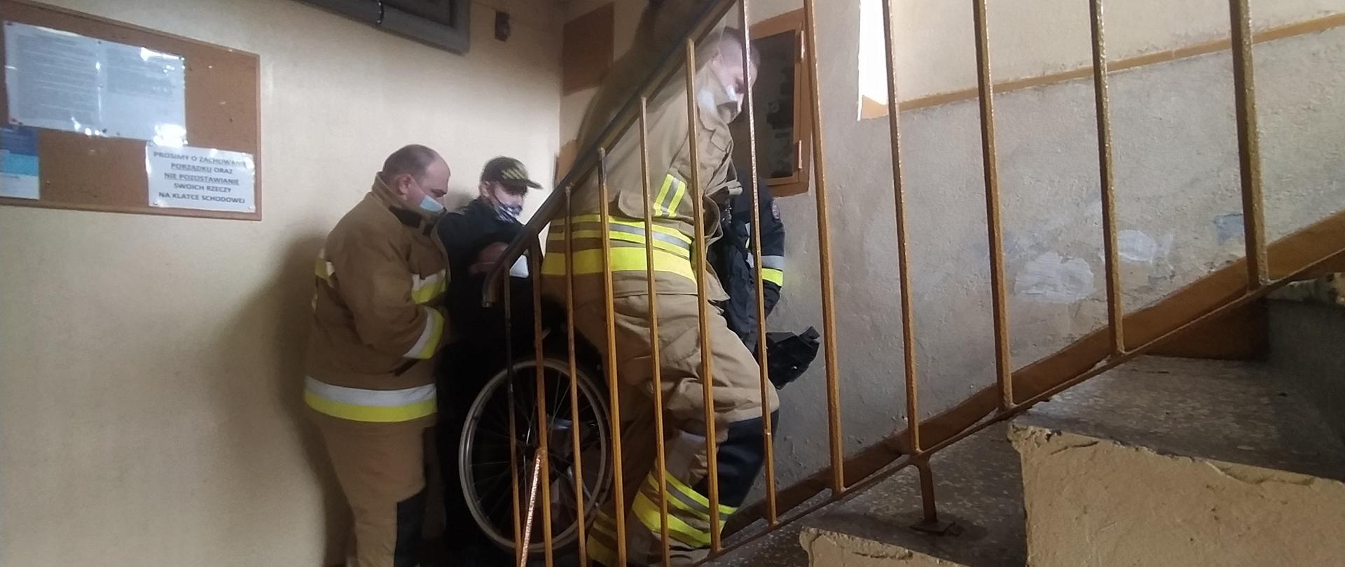 Strażacy pomagaja osobie niepełnosprawnej w transporcie po schodach