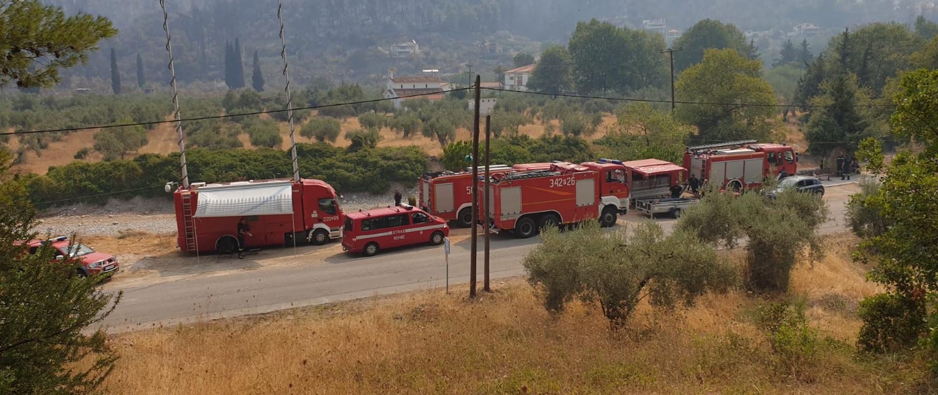 Zdjęcie przedstawia pojazdy pożarnicze podczas postoju przy drodze w trakcie przygotowań do działań.