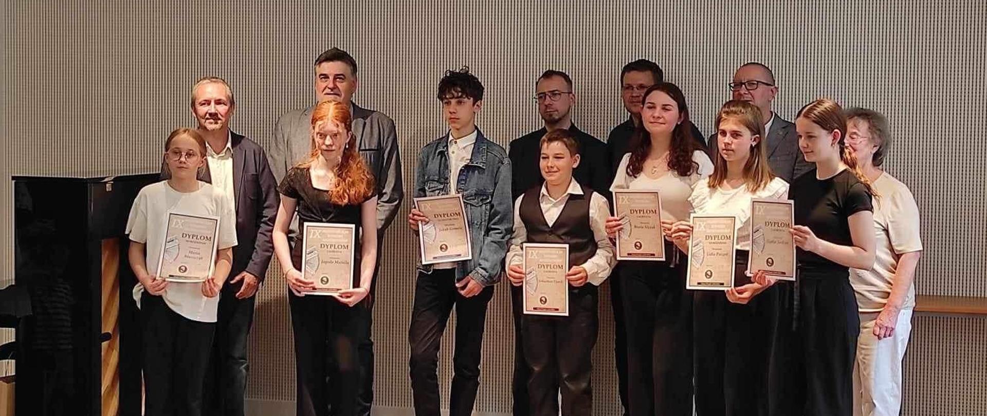 Laureaci konkursu akordeonowego w Nowym Tomyślu stoją z wręczonymi plakatami na tle akustycznej ściany. 