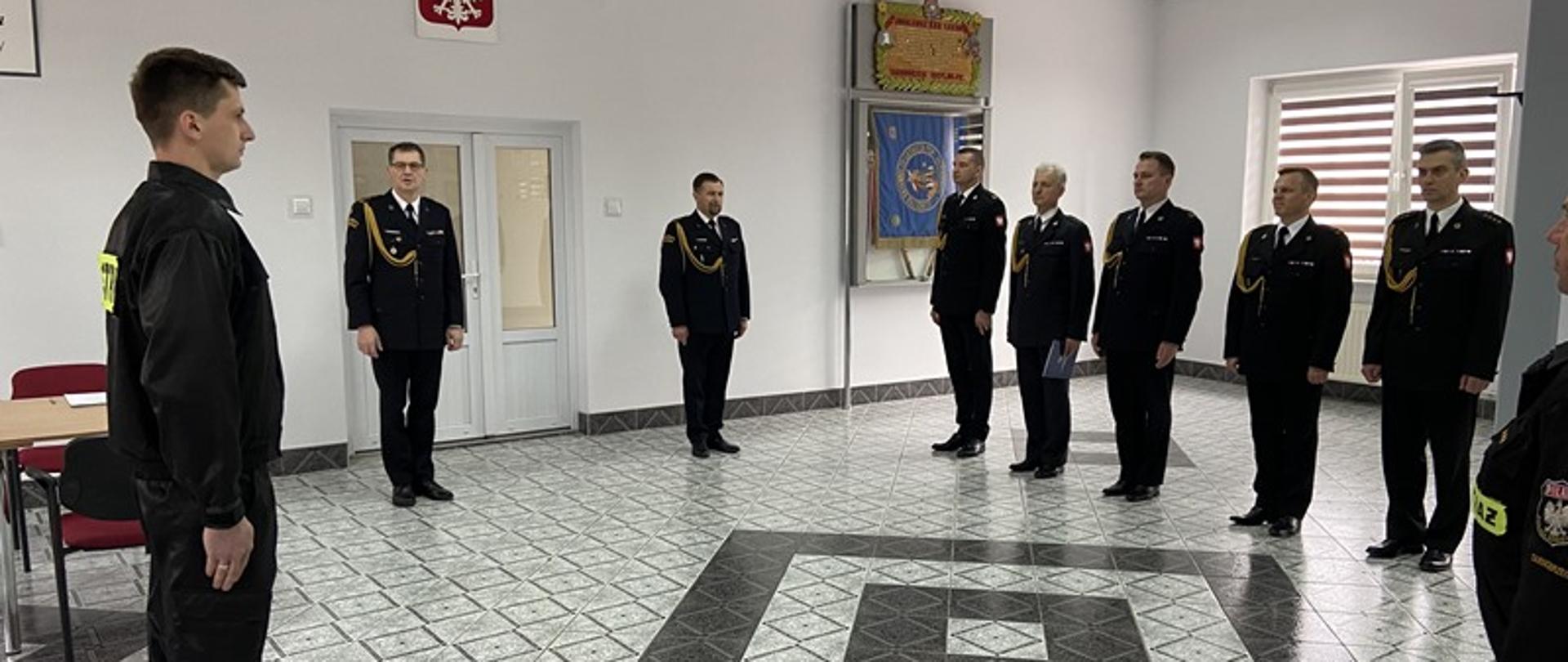 W pomieszczeniu na zbiórce stoją strażacy.