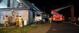 Widoczne pojazdy gaśnicze i podnośnik przy spalonym budynku mieszkalnym , w koło pracujący strażacy