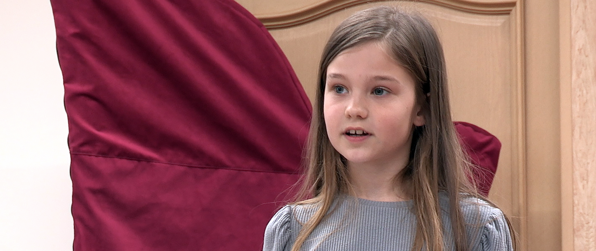 Na zdjęciu dziewczynka patrząca w prawą stronę kadru, w tle ściana z drzwiami.