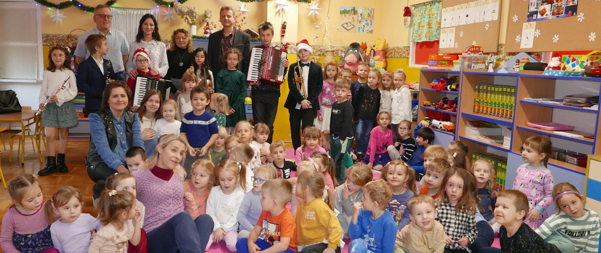 Zdjęcie grupowe przedszkolaków, uczniów szkoły muzycznej którzy trzymają swoje instrumenty, nauczycieli oraz pedagogów.