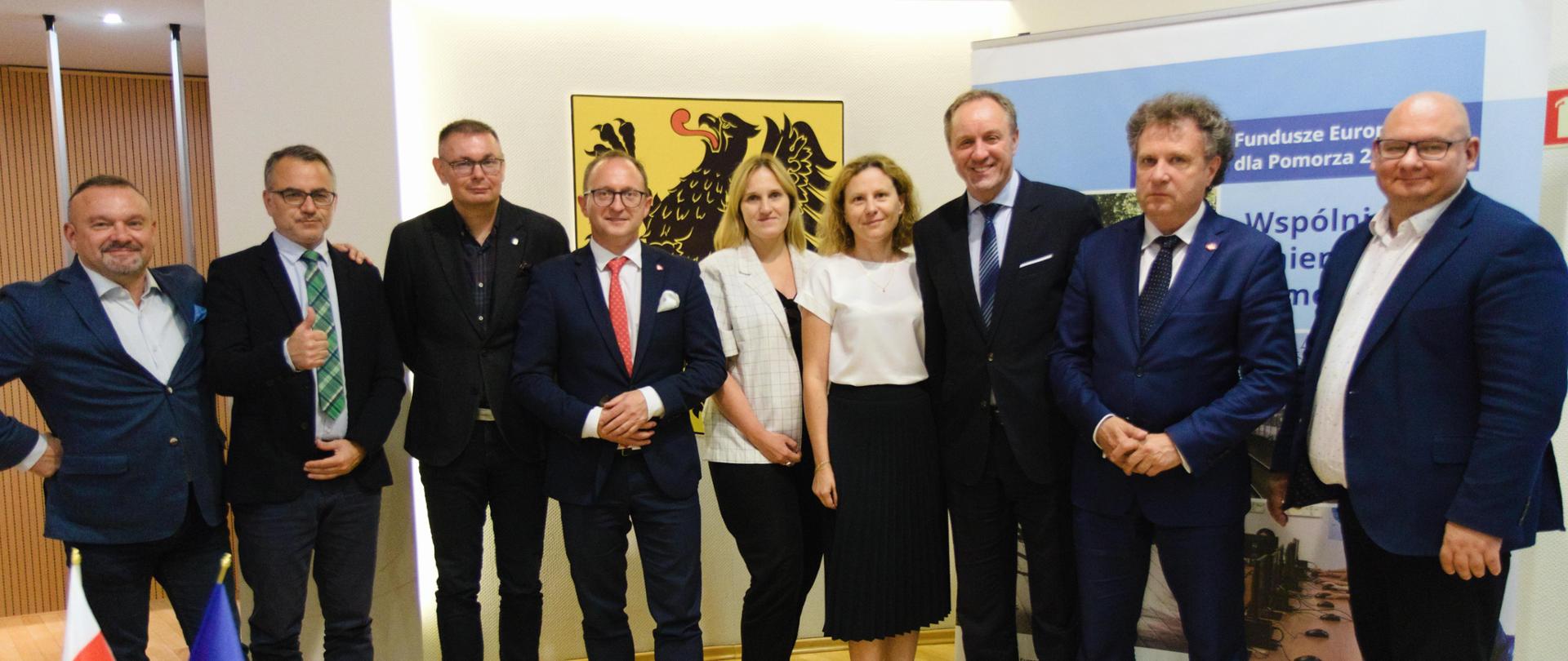 Grupa osób stoi obok siebie w rzędzie. Drugi od prawej stoi wiceminister Jacek Karnowski.