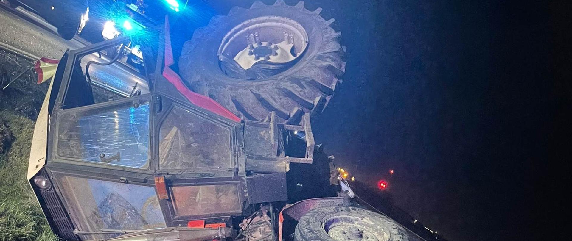 Zdjęcie w porze nocnej. Na zdjęciu uszkodzony pojazd. Zdjęcie na drodze publicznej. Oświetlenie sztuczne. W tle pole uprawne.