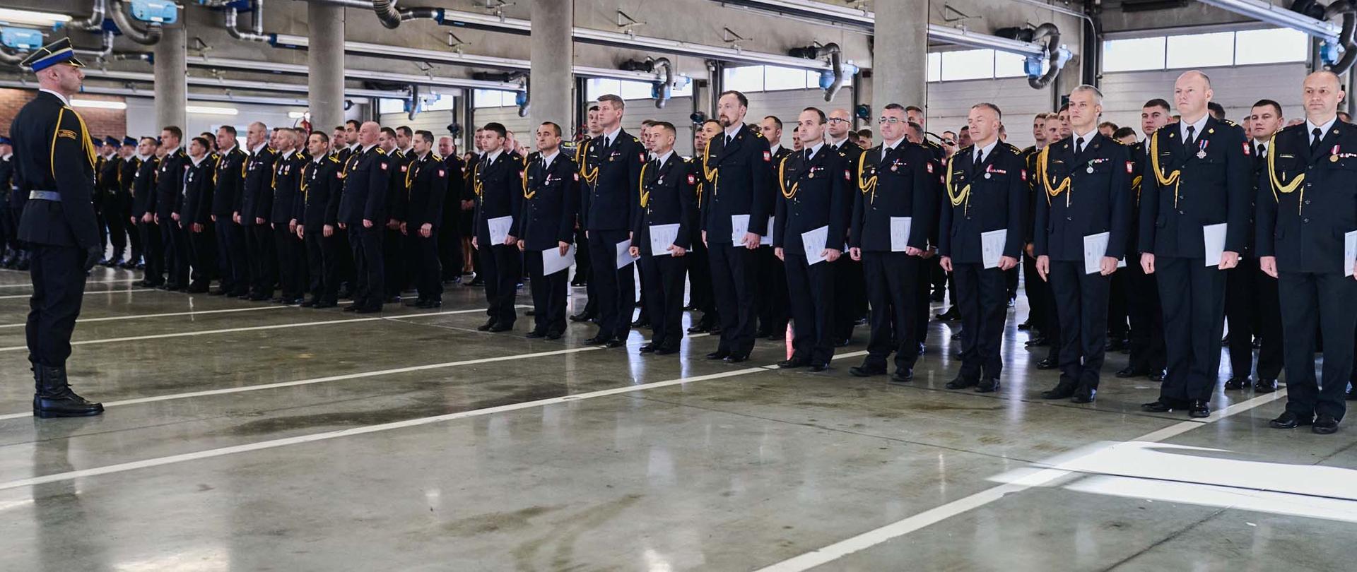 Funkcjonariusze w PSP w mundurach galowych ze sznurem stojący w szyku podczas uroczystości z okazji Wojewódzkich Obchodów Narodowego Święta Niepodległości