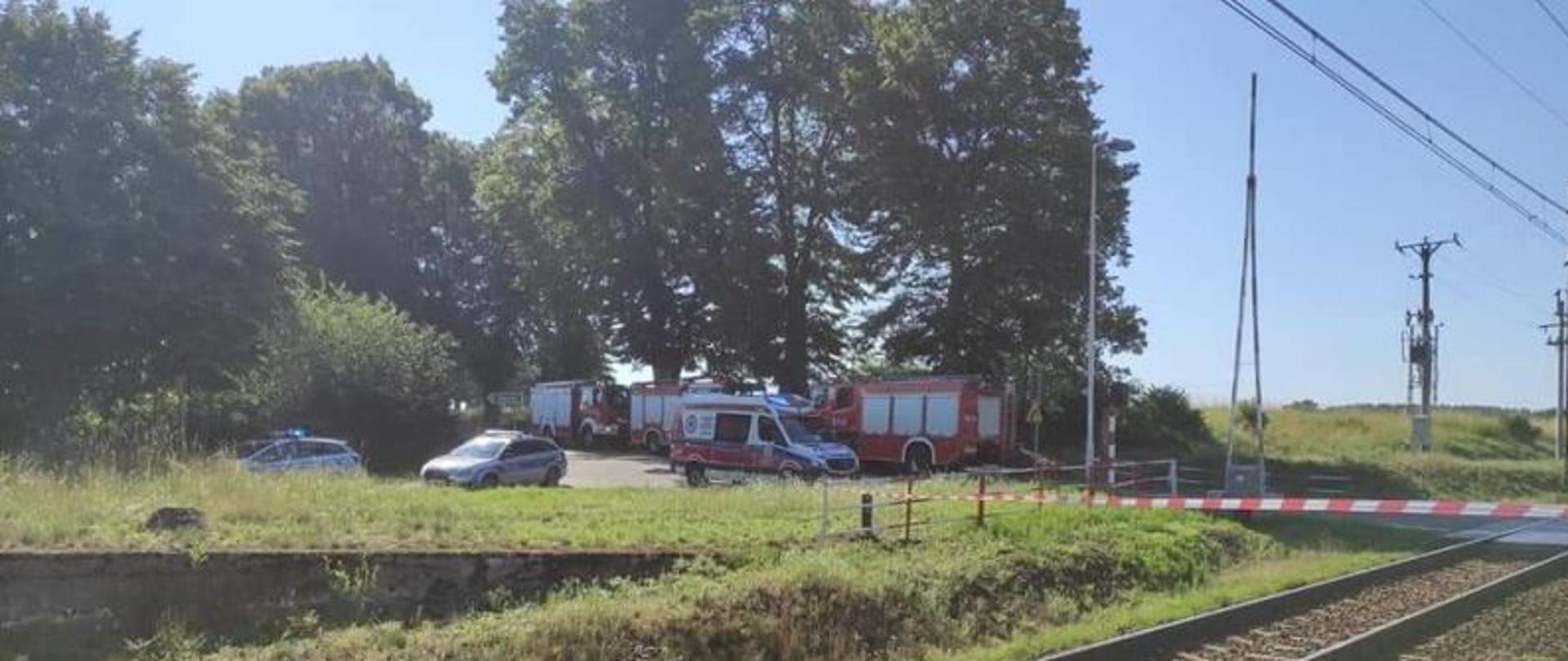 Zdjęcie przedstawia przejazd kolejowy i stacje w Czarnowęsach. W oddali służby ratownicze. Na pierwszym planie taśma ostrzegawcza przecinająca tory.