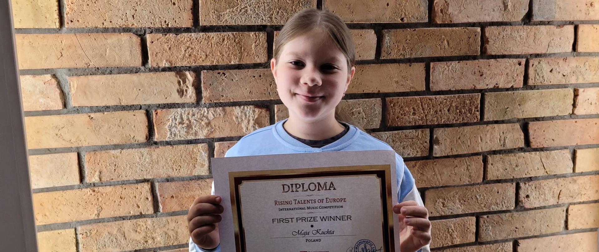 Uczennica trzyma w ręku dyplom na tle ceglanej ściany