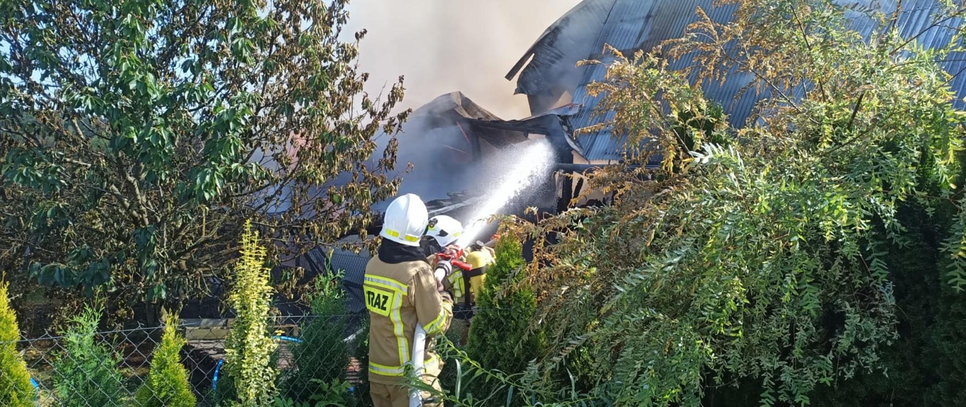 Strazacy podają prąd wody na budynek gospodarczy