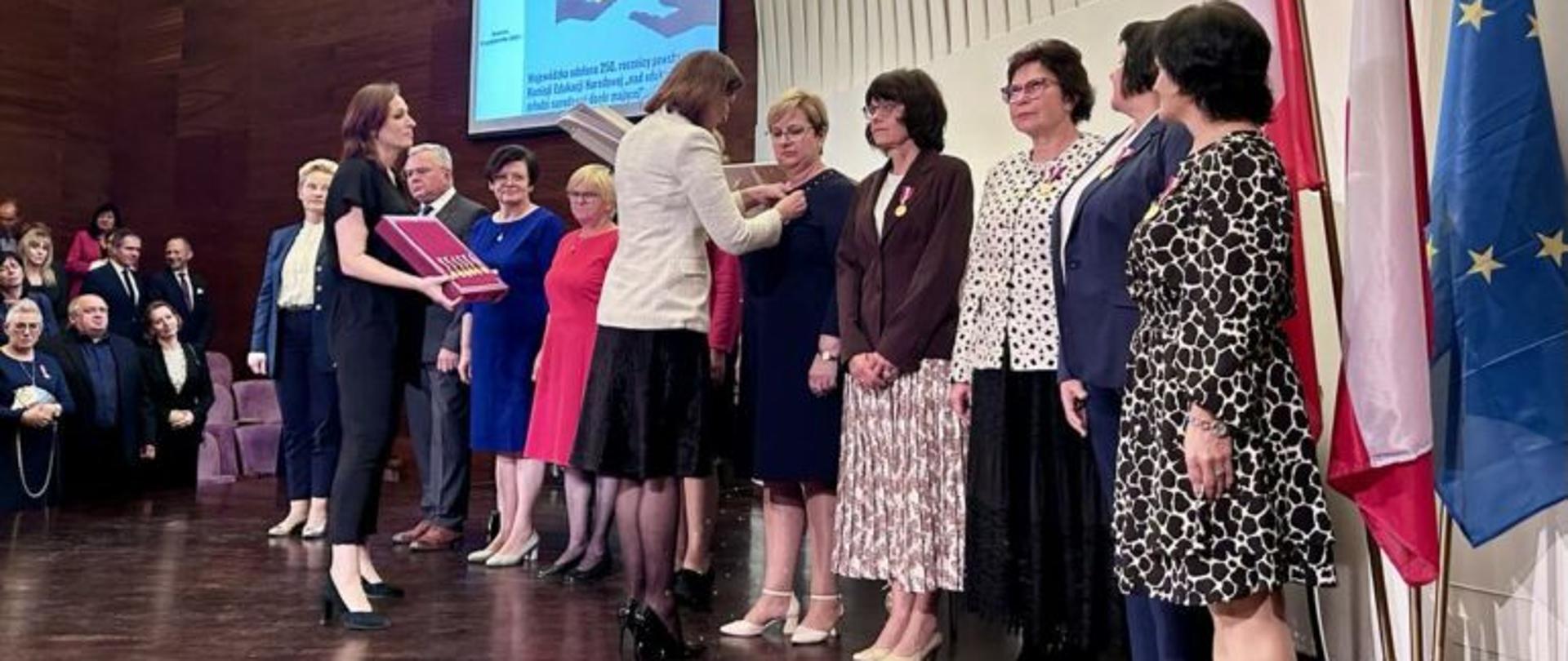 Grupa osób na scenie odbiera odznaczenia państwowe