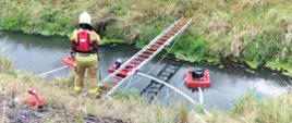 Zdjęcie przedstawia strażaka który podczas ćwiczeń buduje punkt czerpania wody z rzeki.