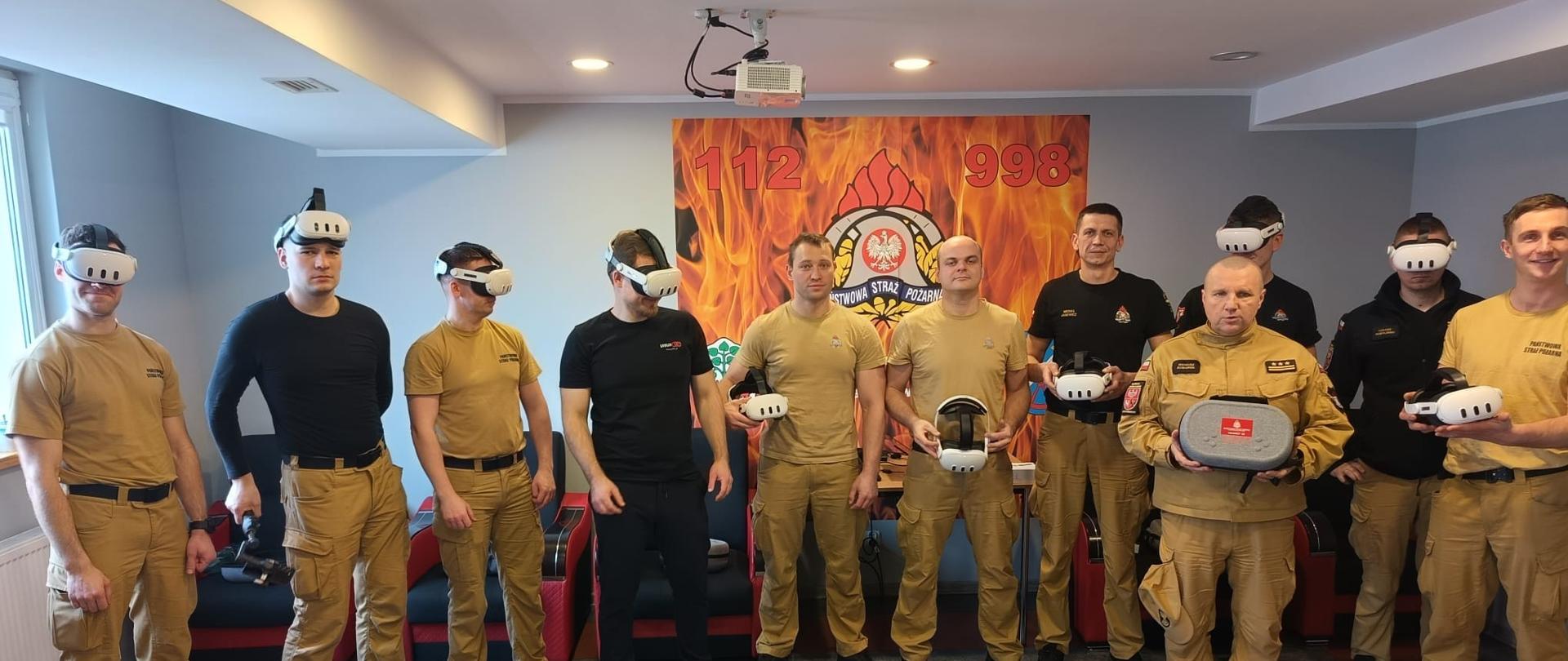 Grupa strażaków na sali szkoleniowej. Część strażaków z okularami do wirtualnej rzeczywistości na głowie.