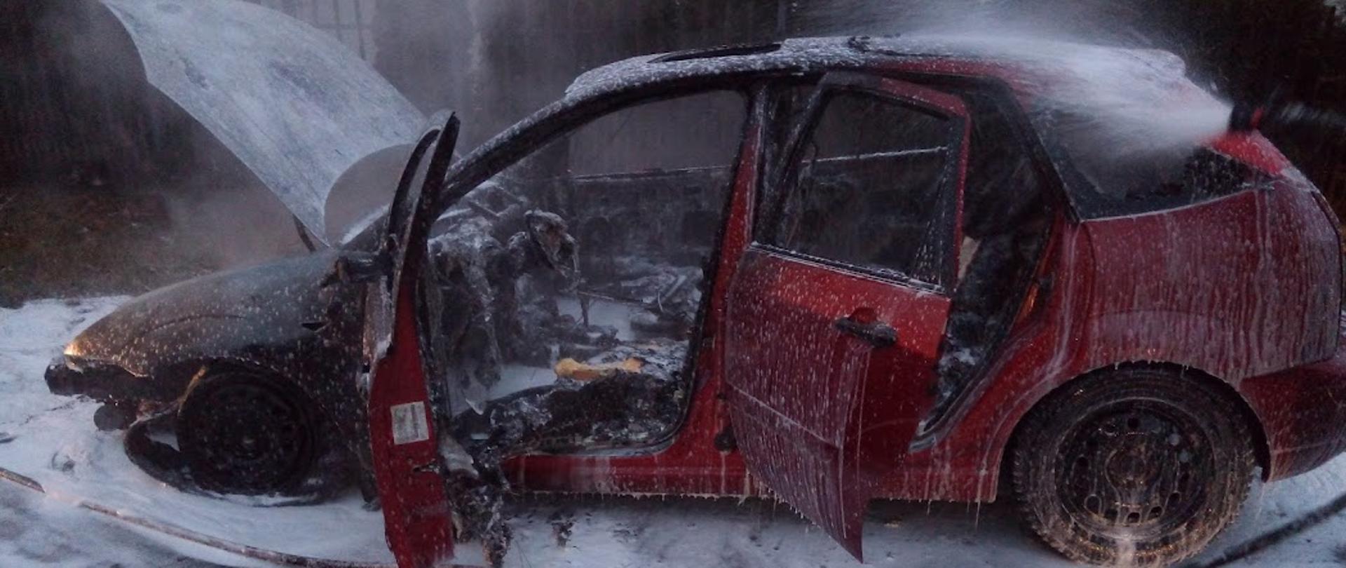 Zdjęcie przedstawia spalony samochód koloru czerwonego gaszony pianą ciężką 