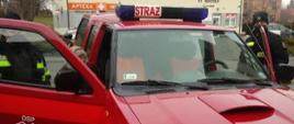 Na zdjęciu widać samochód osobowy OSP Pruchnik III, do którego wsiada starsza kobieta. Po obu stronach pojazdu stoją strażacy OSP.