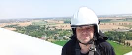 Zdjęcie przedstawia strażaka siedzącego na szczycie wiatraka